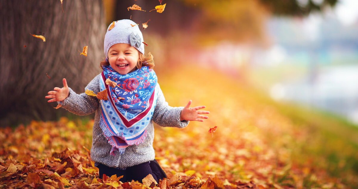 child playing with leaves in the autumn